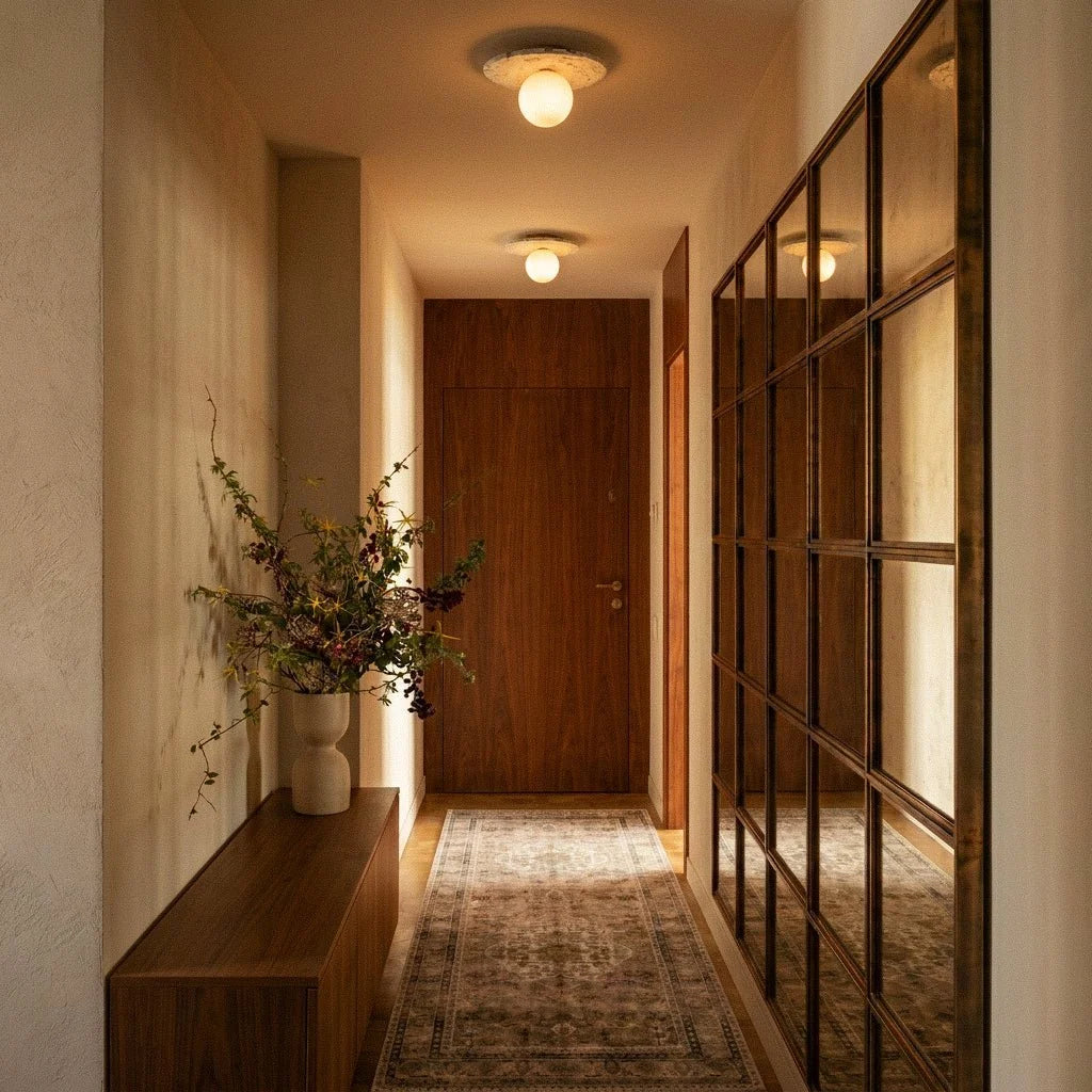 Two terrazzo ceiling lights glow along a wood-panelled hallway leading to a walnut door and mirror, Clérachic lifestyle shot.
