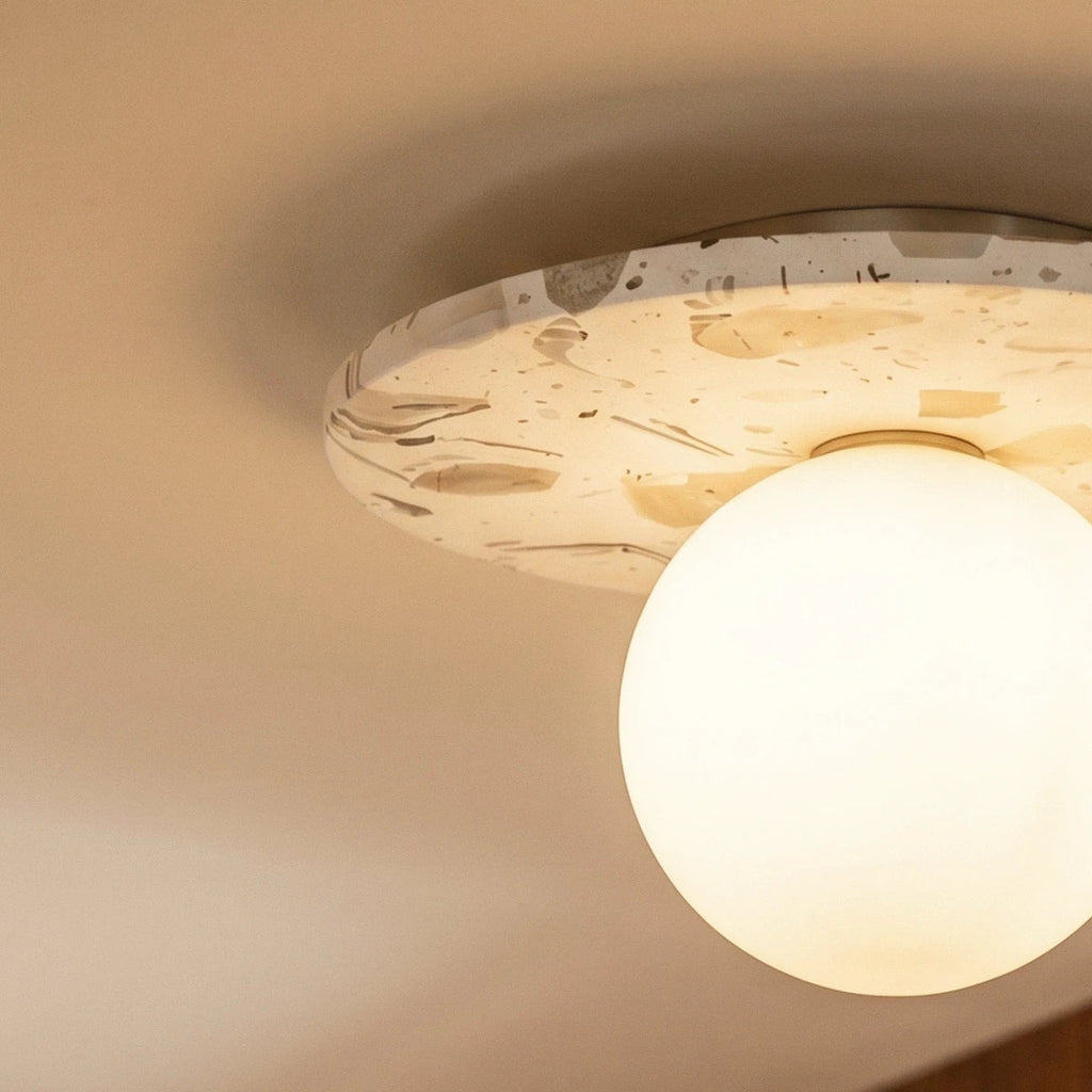 A close-up on the terrazzo disc's flecked pattern and glowing opal globe against a plain ceiling, Clérachic detail shot.