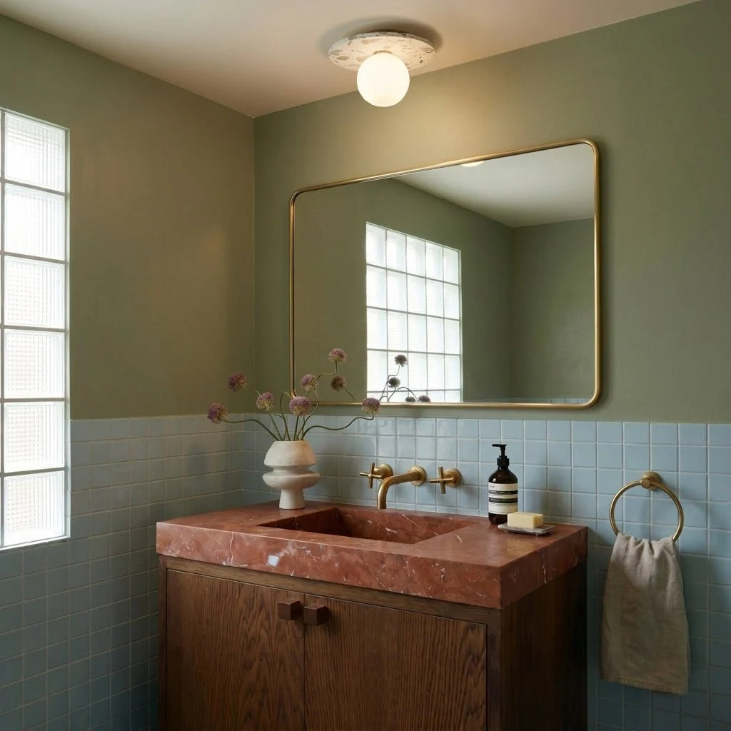 The terrazzo ceiling light glows above a sage-green bathroom with a brass mirror and rose-marble vanity, Clérachic lifestyle shot.