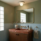 The terrazzo ceiling light glows above a sage-green bathroom with a brass mirror and rose-marble vanity, Clérachic lifestyle shot.