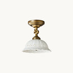 Clérachic flush-mount ceiling light with an antique brass swivel arm and a white ceramic dome shade pierced with a scalloped lace pattern, on white.