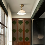 This Clérachic brass and ceramic ceiling light hanging in front of a tall wooden cabinet with green diamond-patterned glass panels.
