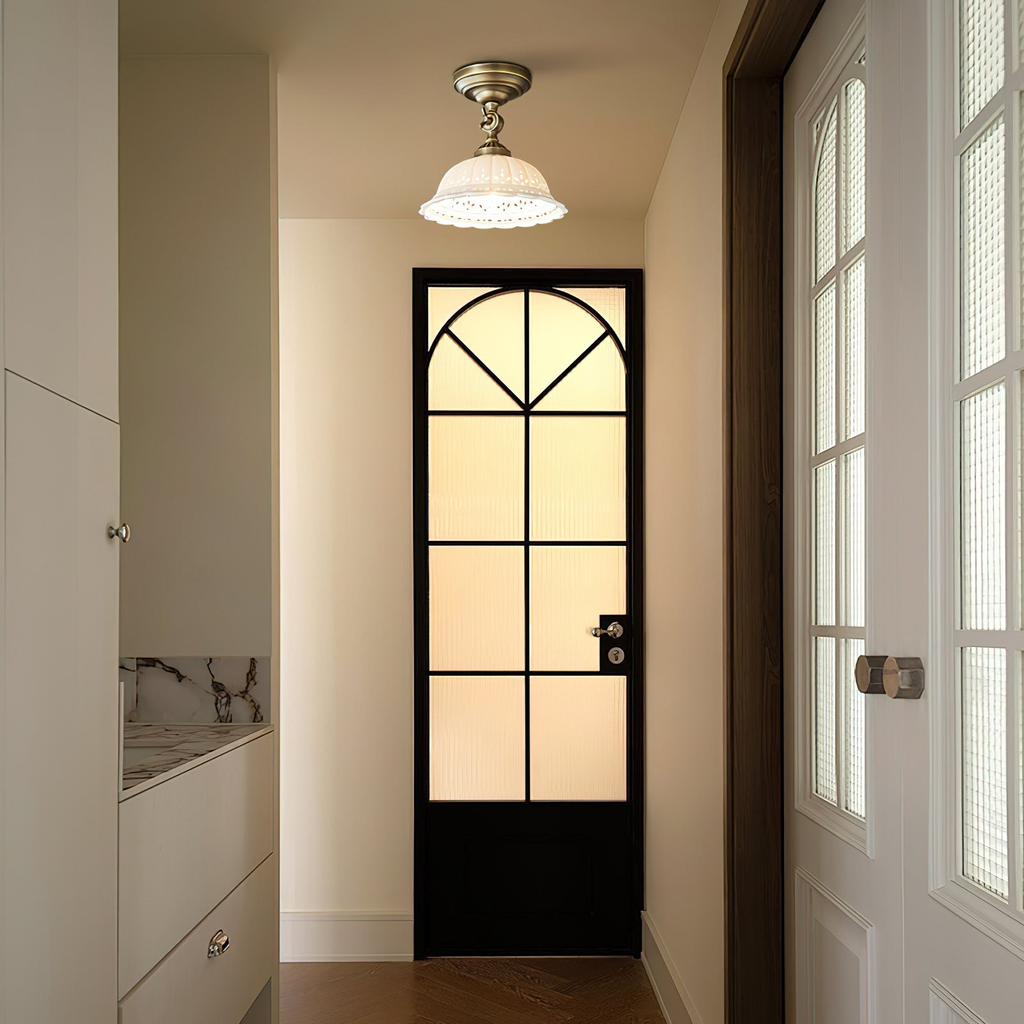 Brass-armed ceramic ceiling light from Clérachic in a doorway, with a black-framed glazed door and a frosted pane behind it.