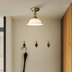 A Clérachic ceramic dome light above a small cloakroom wall with three brass hooks and a folded black umbrella.