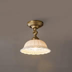 Lit Clérachic ceramic dome light on a brass swivel arm against a grey wall, the scalloped pierced rim glowing warm.
