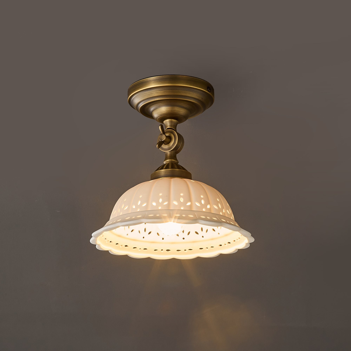 Straight-on view of the lit Clérachic ceramic dome and brass canopy against a grey wall, with soft light spilling below.
