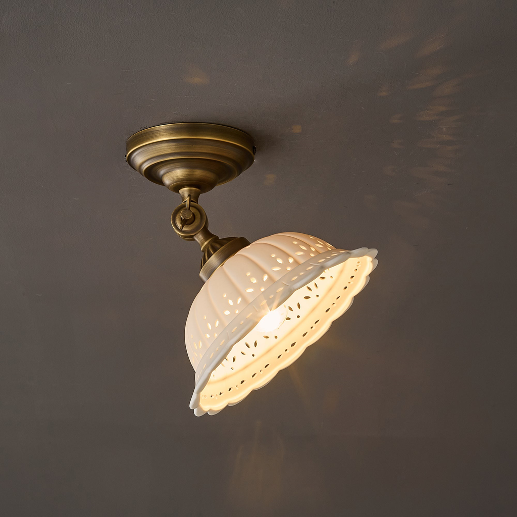 The same Clérachic ceramic dome tilted on its brass joint and lit, with a scatter of light patterns cast across the grey wall behind.