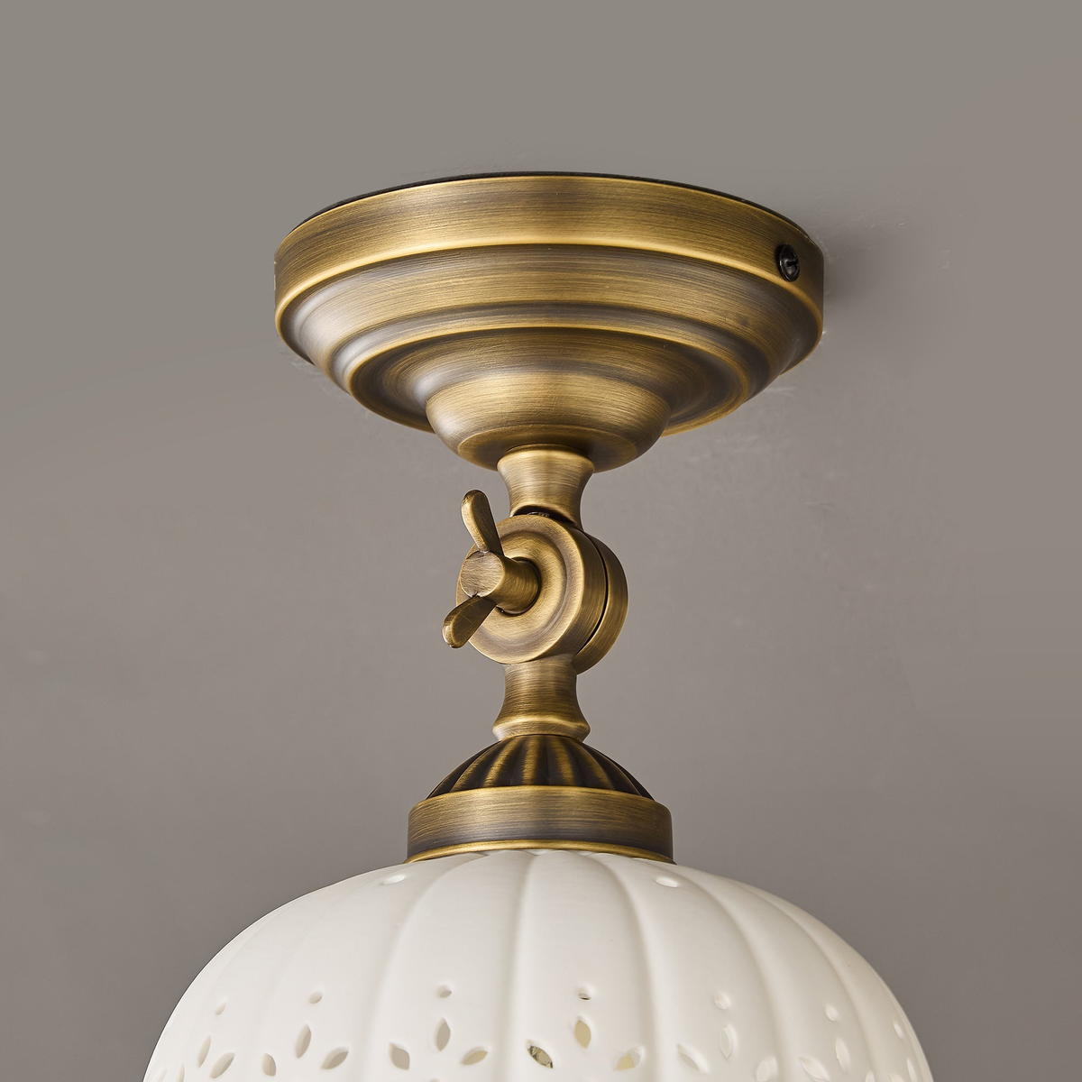 Close view of the layered brass canopy and the wing-nut swivel joint above the ceramic dome of this Clérachic ceiling light.