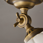 Extreme close view of the brass wing-nut swivel joint and ribbed collar on this Clérachic ceiling light, with the ceramic dome below.