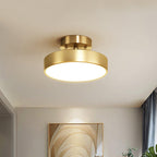 A Clérachic brass ceiling light lit above an entry hall, with a framed arched artwork on the wall below and grey curtains beside.