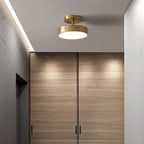 A brass Clérachic ceiling light above a hallway of walnut-veneer doors, with a strip of light along the ceiling edge.