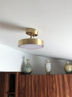 Clérachic brass ceiling light with its head tilted, set beneath a sloping ceiling above a wooden cabinet and three vases.