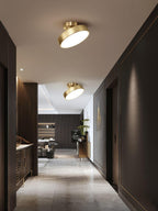 A Clérachic brass ceiling light turned at an angle in a long hallway with dark wall panels and a stone-effect floor.