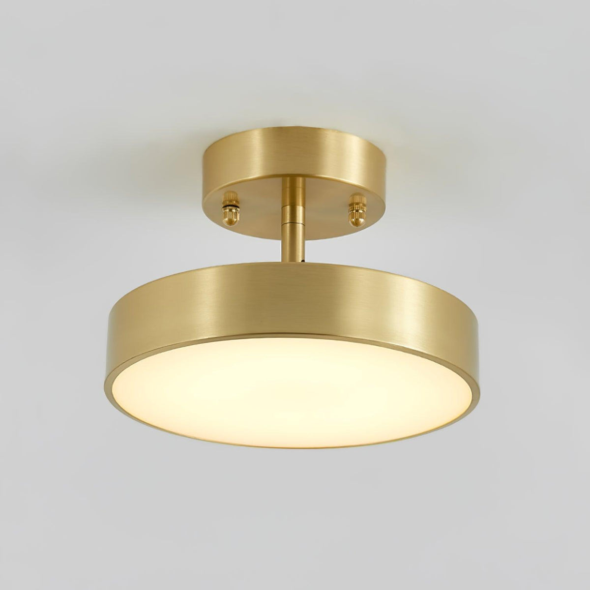 Close view of the Clérachic brass ceiling light, with its brushed metal canopy, thin stem and softly lit round diffuser.