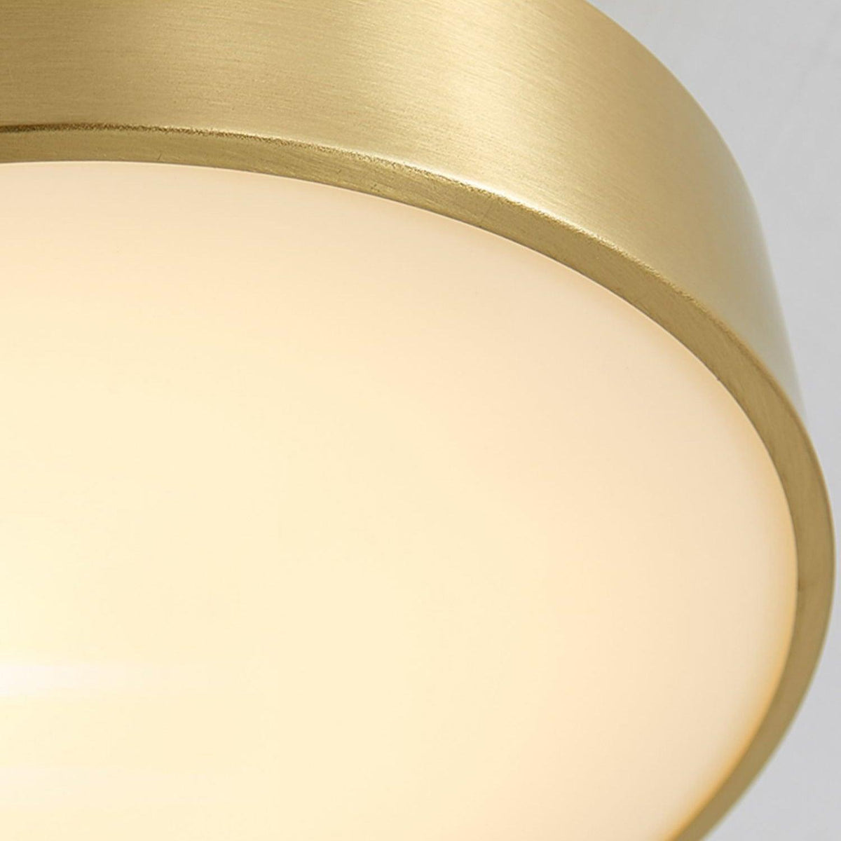 Close view of the lit diffuser and brass edge on this Clérachic ceiling light, the glow soft and even across the disc.