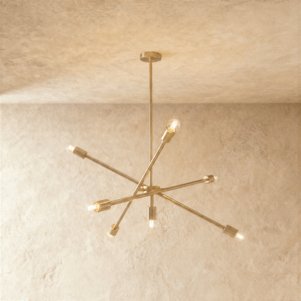 Clérachic sputnik-style chandelier in polished brass with crossed arms, hung from a plaster ceiling in studio light.