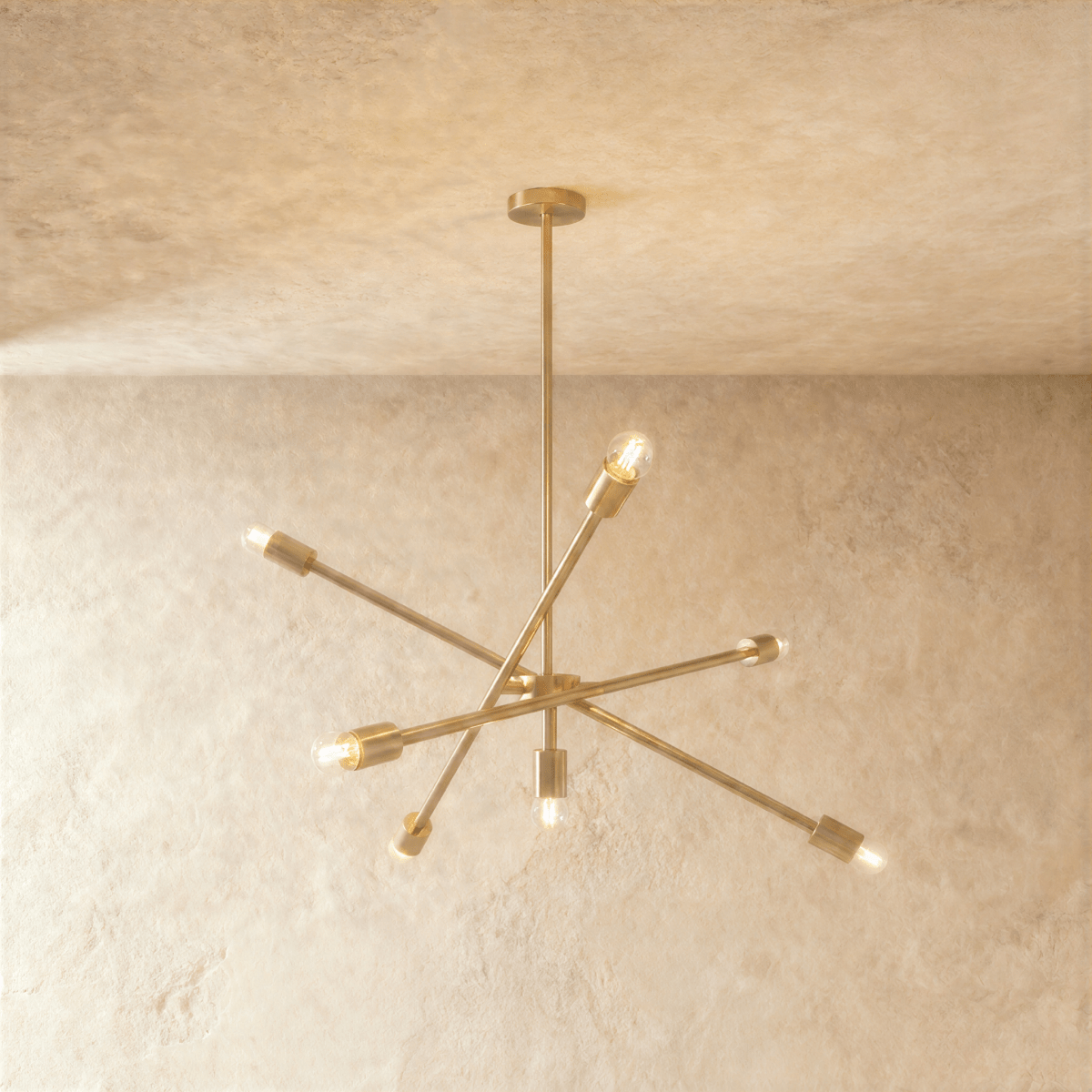 Clérachic sputnik-style chandelier in polished brass with crossed arms, hung from a plaster ceiling in studio light.