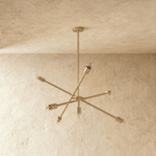 Clérachic sputnik-style chandelier in polished brass, shown from a slightly closer studio angle on a plaster wall.