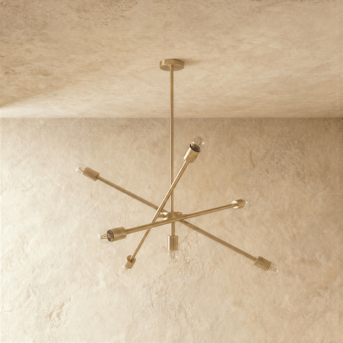 Clérachic sputnik-style chandelier in polished brass, shown from a slightly closer studio angle on a plaster wall.