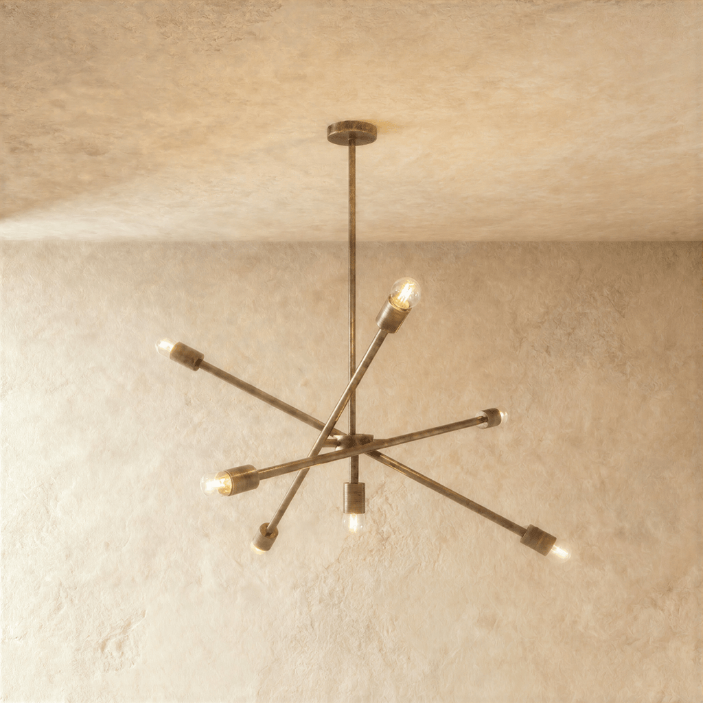 Clérachic sputnik-style chandelier in vintage brass with crossed arms, hung from a plaster ceiling in studio light.