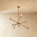 Clérachic sputnik-style chandelier in vintage brass with crossed arms, hung from a plaster ceiling in studio light.