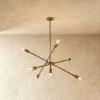 Clérachic sputnik-style chandelier in vintage brass with crossed arms, hung from a plaster ceiling in studio light.