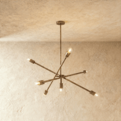 Clérachic sputnik-style chandelier in vintage brass with crossed arms, hung from a plaster ceiling in studio light.