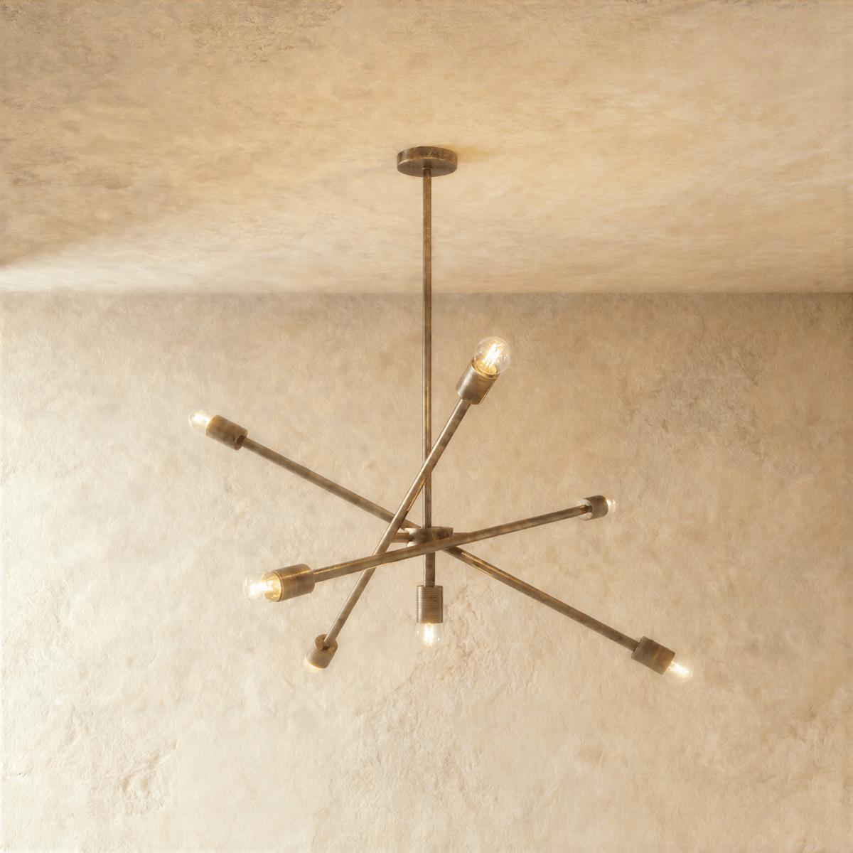 Clérachic sputnik-style chandelier in vintage brass with crossed arms, hung from a plaster ceiling in studio light.