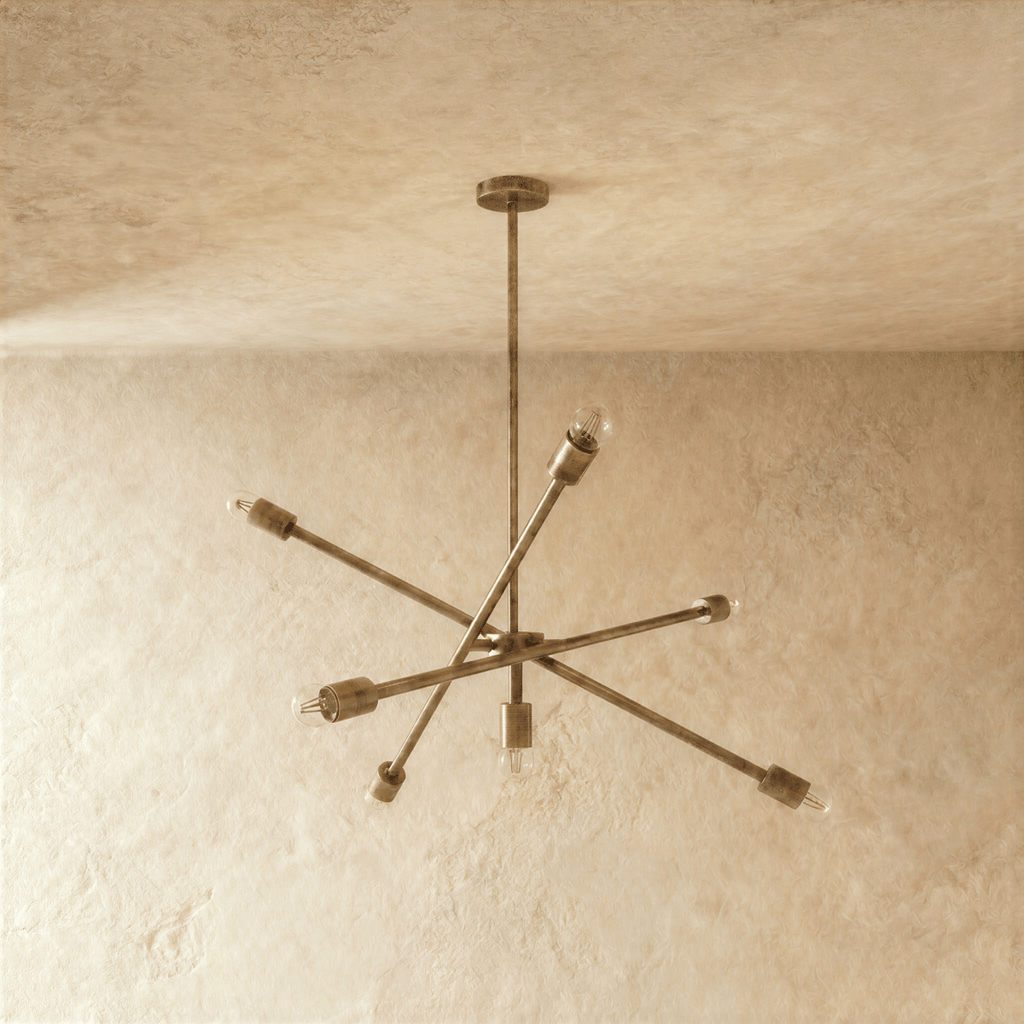 Clérachic sputnik-style chandelier in vintage brass, shown from a slightly closer studio angle on a plaster wall.