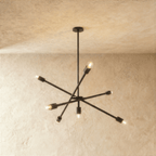 Clérachic sputnik-style chandelier in matte black with crossed arms, hung from a plaster ceiling in studio light.