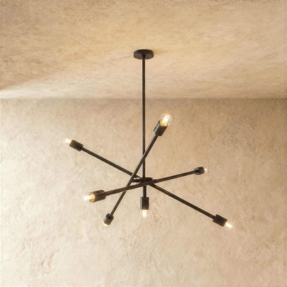 Clérachic sputnik-style chandelier in matte black with crossed arms, hung from a plaster ceiling in studio light.