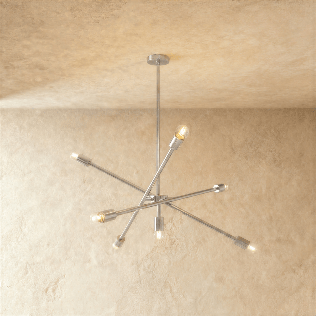 Clérachic sputnik-style chandelier in chrome with crossed arms, hung from a plaster ceiling in studio light.