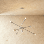 Clérachic sputnik-style chandelier in chrome with crossed arms, hung from a plaster ceiling in studio light.