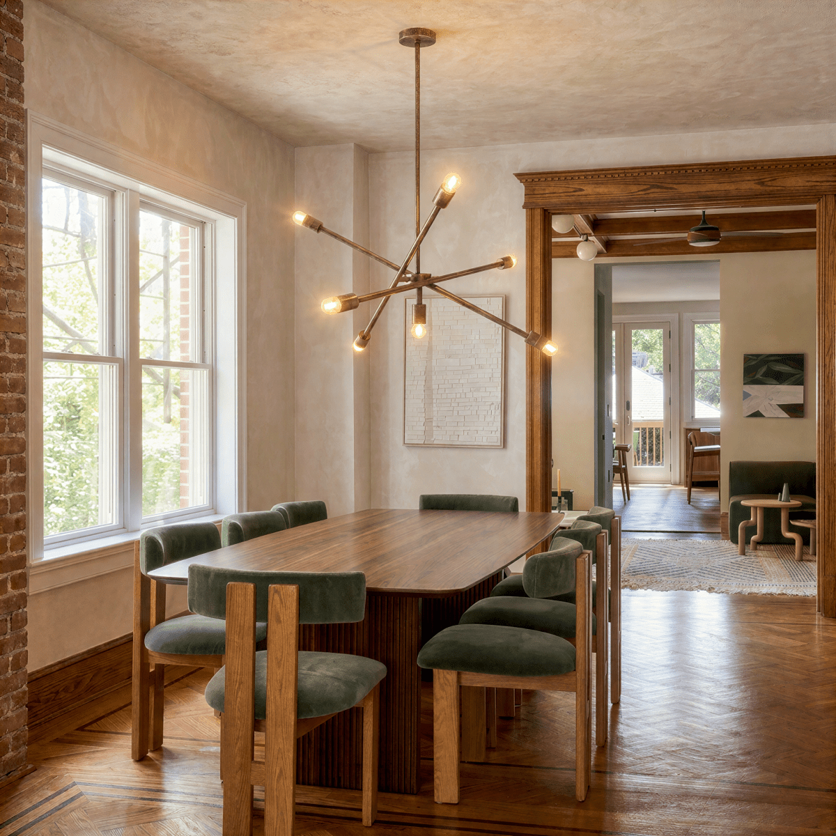 Clérachic vintage brass sputnik chandelier lit above a long dining table in a house with an exposed brick wall.