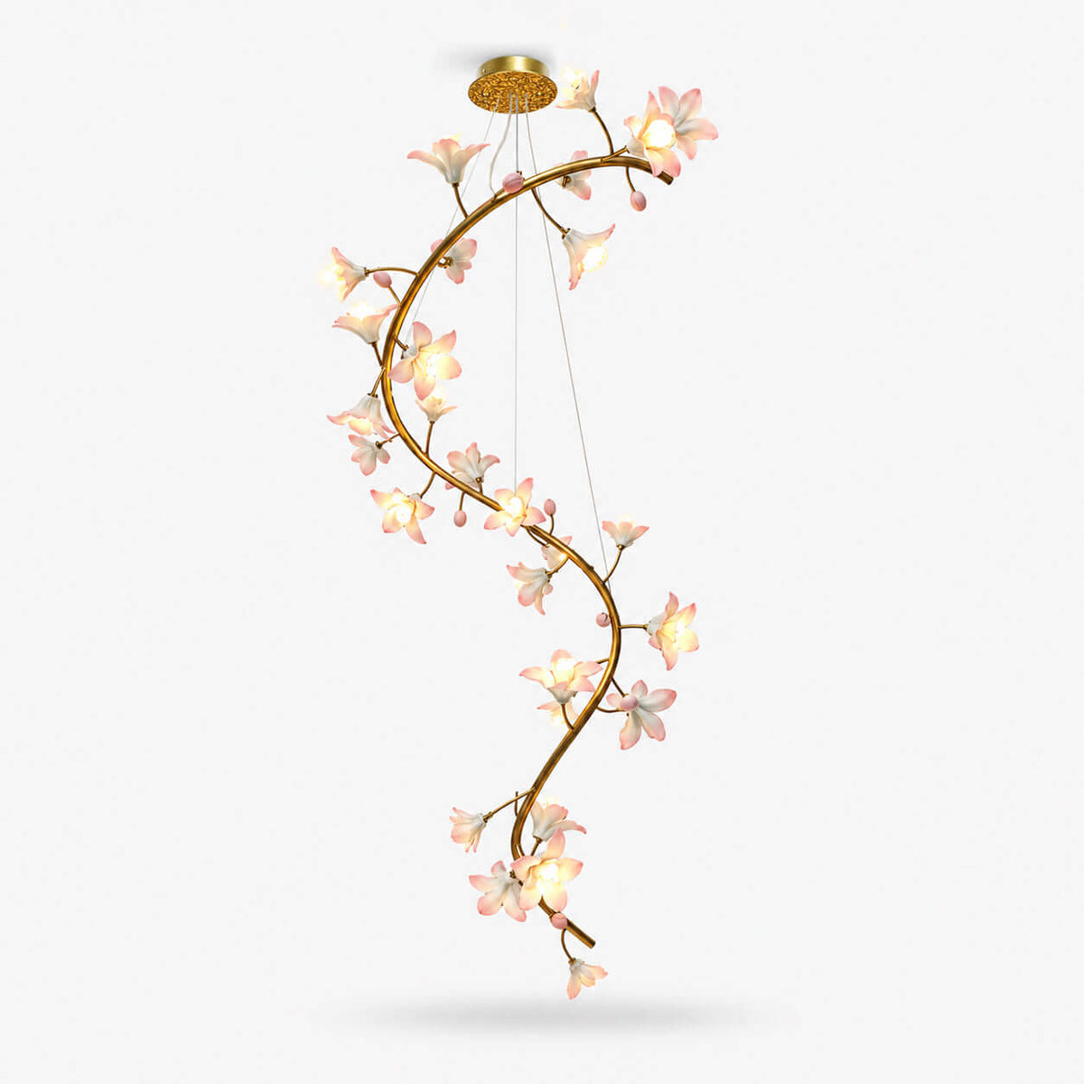 Clérachic chandelier on a white backdrop, a long S-curved brass vine hung from a gold canopy and covered in lit pink-white ceramic blooms.