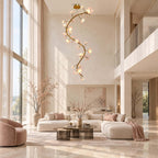 Tall Clérachic chandelier glowing under a high ceiling above a pale sofa, a pink armchair and a vase of blossom branches.