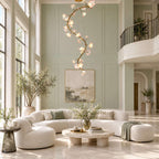 Clérachic chandelier lit against a sage-green panelled wall, above a boucle sofa, a stone coffee table and an olive tree.