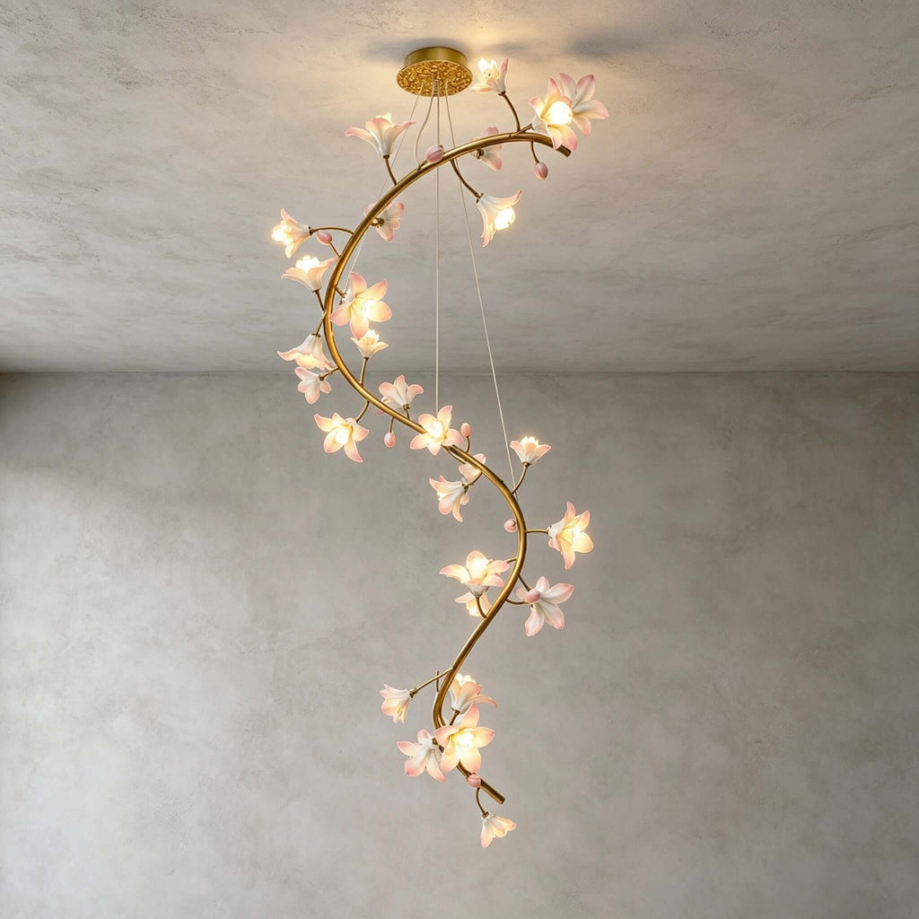 Full view of this Clérachic chandelier lit in an empty room with a grey plaster wall, the brass vine curving down from its gold canopy.