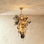 Clérachic brass chandelier with a tall cluster of faceted amber and smoked glass shapes lit warm, hanging from a slim chain and canopy.
