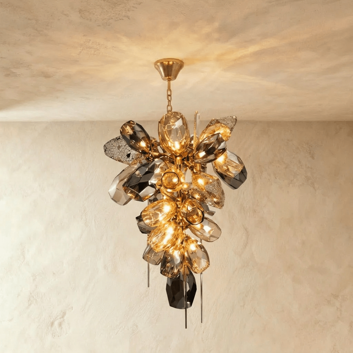 Clérachic brass chandelier with a tall cluster of faceted amber and smoked glass shapes lit warm, hanging from a slim chain and canopy.