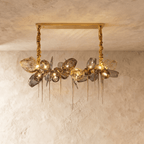 Clérachic linear chandelier with smoked glass shades and brass mesh pieces, hung from two gold fabric-wrapped chains on a bar canopy.