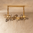 Clérachic wide linear chandelier on a brass bar, with smoked glass, brass lattice shades and long tapered spikes over a limewash wall.