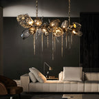Clérachic linear chandelier in smoked glass and brass lattice, hung from chains over a cream sofa and a dark panelled wall.