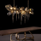 Clérachic linear brass and smoked glass chandelier with spiked drops, lit above a live-edge wooden table on a brass base.