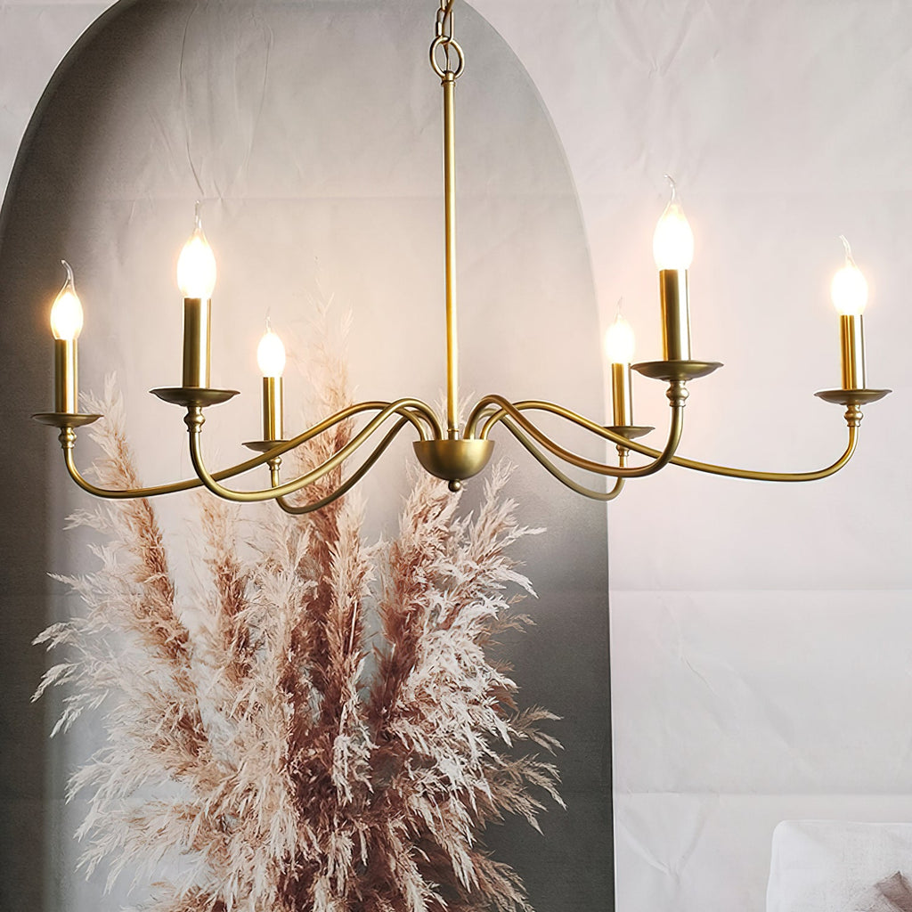 A Clérachic brass chandelier with glowing candle bulbs hangs before an arch and a plume of dried pampas grass.