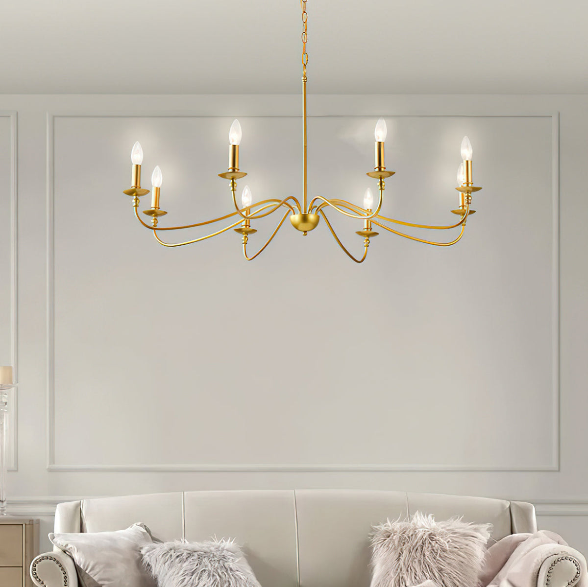 A Clérachic brass chandelier hangs in front of a panelled grey wall, above a cream sofa with fluffy cushions.