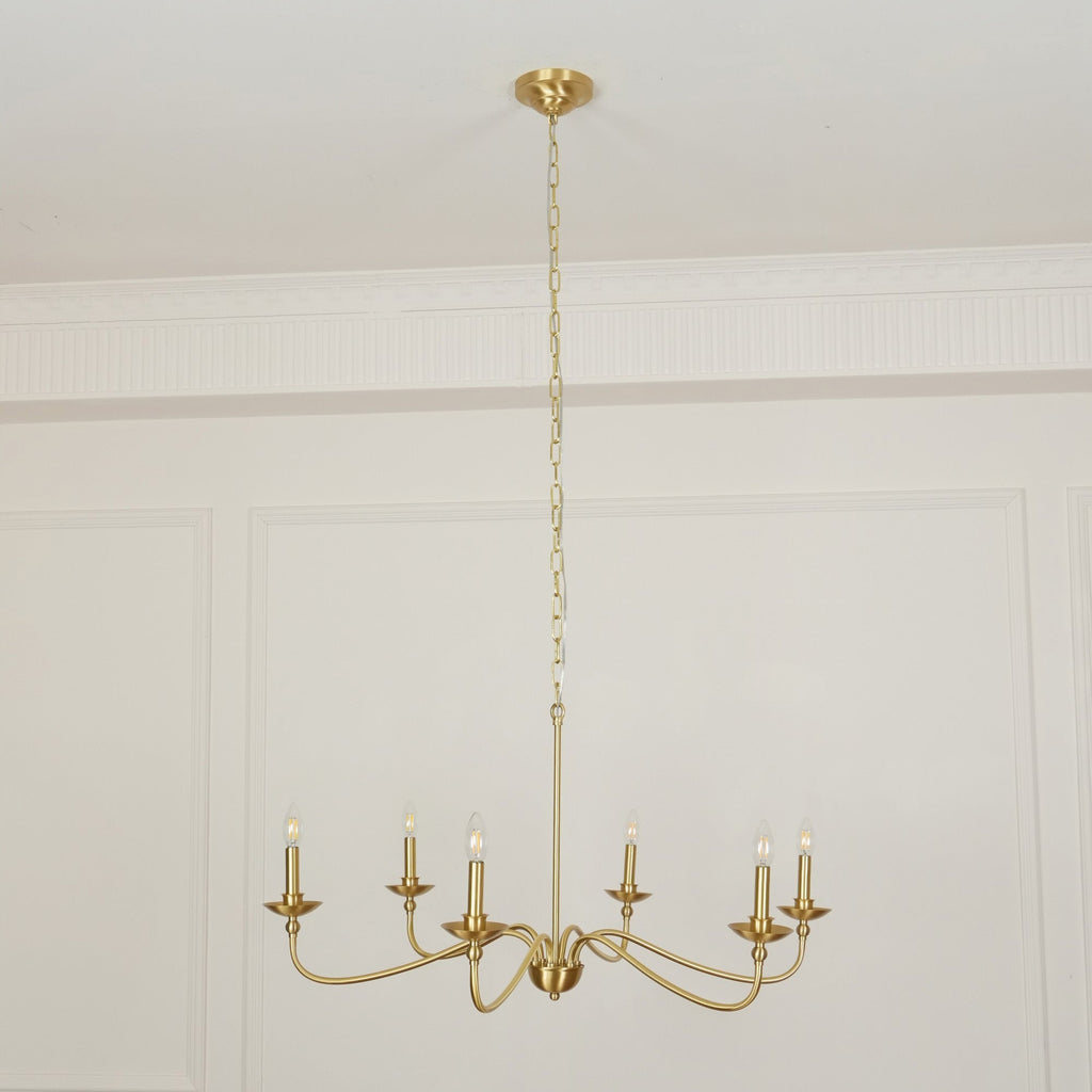 A Clérachic brass chandelier hangs low from a long chain below a panelled ceiling cornice in a pale room.