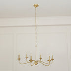 A Clérachic brass chandelier hangs low from a long chain below a panelled ceiling cornice in a pale room.