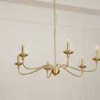 A Clérachic brass chandelier shown from below, its curved arms, small dishes and candle bulbs, seen against a panelled wall.