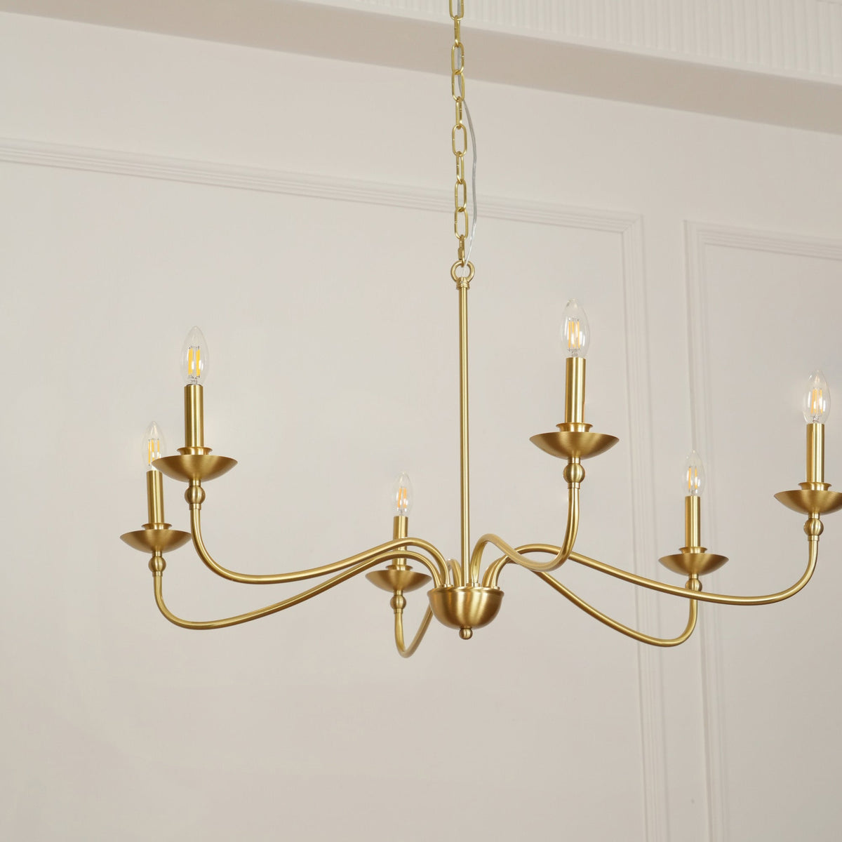 A Clérachic brass chandelier shown from below, its curved arms, small dishes and candle bulbs, seen against a panelled wall.